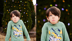 Young child with serious expression wearing green long-sleeve shirt with graphic design, photographed against blurred bokeh background.