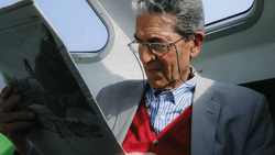 Man in blazer and red cardigan reviewing tablet outdoors near aircraft.