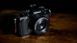 Nikon Zf mirrorless camera with attached lens on wooden surface against dark background.