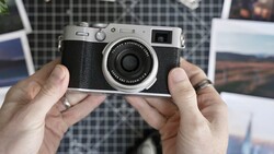 Hands holding a silver and black rangefinder camera with fixed lens against a plaid background.
