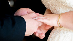 Bride and groom exchanging rings during wedding ceremony, showing their clasped hands with wedding bands visible.