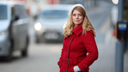 Woman in red coat standing on urban street with blurred cars in background.