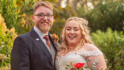 Bride and groom smiling outdoors during golden hour with lush greenery in the background.