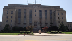 Symmetrical Art Deco government building with tan stone facade, central clock tower, and manicured landscaping.