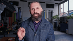 Bearded man in denim shirt gesturing while speaking in a studio workshop.