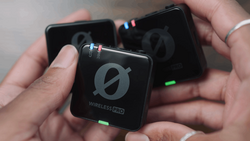 Three compact wireless audio transmitter units held in hands, displaying illuminated status indicators and branded logos.