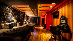 Luxury hotel bedroom with dramatic red and gold lighting, quilted headboard, and ornate mirror at vanity.