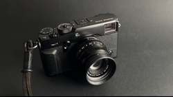 Black rangefinder camera with leather strap on dark gray background.
