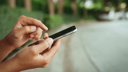 Hands holding a smartphone outdoors with blurred garden background.