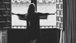 Woman with arms outstretched silhouetted against open double doors in a dramatic black and white composition.