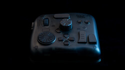 Gaming controller with analog stick, directional pad, and button layout displayed against dark background with blue rim lighting.