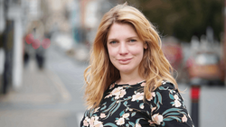 Woman with strawberry blonde hair wearing a floral patterned top, photographed outdoors on a city street.