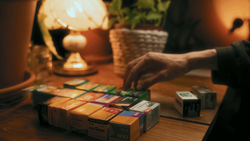 Hand selecting from a color swatch palette on a wooden desk under warm lamp light.