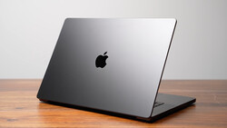 Space gray MacBook Pro closed on wooden surface against neutral background.