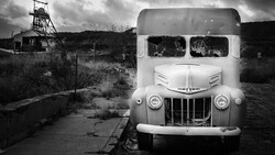 Abandoned truck with broken windows at a derelict mining site with headframe visible in background.