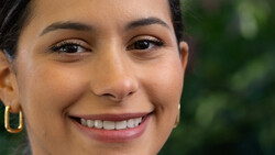 Close-up portrait of a woman smiling at the camera with natural outdoor lighting.