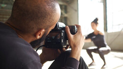 Photographer holding a cinema camera filming a dancer in a bright studio space.