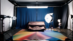 Professional photography studio setup with gradient floor, blue curtain backdrop, and multiple studio lights.