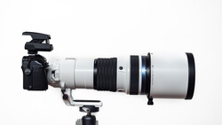 Professional telephoto lens with white barrel mounted on camera body with tripod collar and microphone attachment.