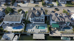 Aerial view of waterfront homes with pools and docks along a residential canal.