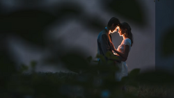 Couple embracing outdoors at dusk with warm backlighting creating a glowing silhouette effect.