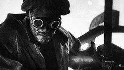 Black and white portrait of a person wearing circular goggles and dark clothing, shot from a low angle.