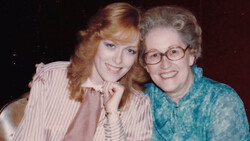 Two women smiling at the camera in a close portrait composition against a dark background.