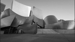 Black and white photograph of a modern curved architectural building with flowing metallic surfaces and angular geometric forms.
