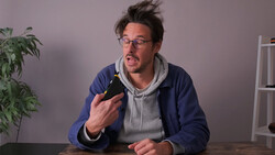 Man in glasses holding a dark bottle while speaking animatedly at a table.