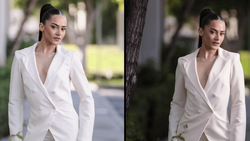 Woman in white blazer photographed outdoors during daytime with natural lighting and blurred foliage background.