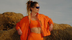 Woman in bright orange athletic wear posing against large boulders in natural daylight.