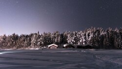 Snow-covered cabins nestled against a forested shoreline under a starry twilight sky.