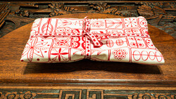 Red and white patterned fabric gift wrapped with twine bow on wooden table with ornate carved border.