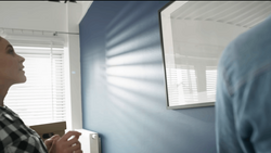 Two people in an interior space with blue walls and bright window light creating linear shadows across the surface.