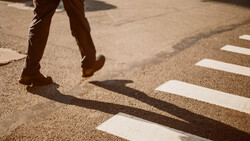 Person's legs and shadow crossing a zebra crossing on pavement in bright sunlight.