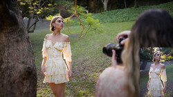 Woman in cream off-shoulder dress standing in garden during outdoor portrait shoot.