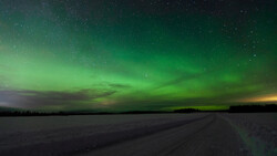 Aurora borealis illuminates the night sky in brilliant green above a frozen landscape and dirt road.