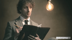 Man in business suit holding tablet with pencil under warm incandescent bulb.