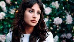 Woman with long dark wavy hair against a blooming flower wall backdrop.
