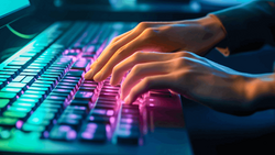 Hands typing on an illuminated mechanical keyboard with neon pink and cyan backlighting.