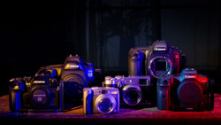 Collection of Canon and Olympus digital cameras illuminated with blue and red LED lighting against a dark background.