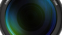Close-up view of a camera lens barrel showing multicoated glass elements with blue and green light reflections.