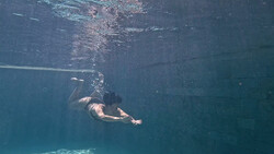 Snorkeler underwater viewed from above, swimming toward the surface with sunlight filtering through the water.