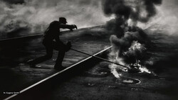 Silhouetted firefighter directing water stream at industrial fire in black and white photograph.