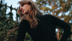 Woman in black long-sleeve top looking over shoulder outdoors during golden hour.