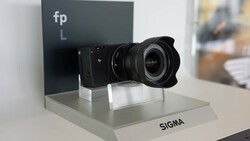 Sigma lens mounted on fp L camera body displayed on white pedestal with branding.