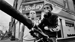 Two young men posing outdoors in front of a storefront with "Today" signage visible above them.