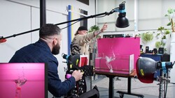Filmmaker operating a professional camera rig with large magenta display monitors and overhead lighting setup.