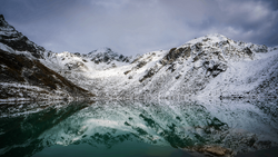 Snow-covered mountain slopes surrounding a turquoise alpine lake under overcast sky.