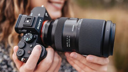 Photographer holding a Sony mirrorless camera with a telephoto lens and external flash mounted on top.